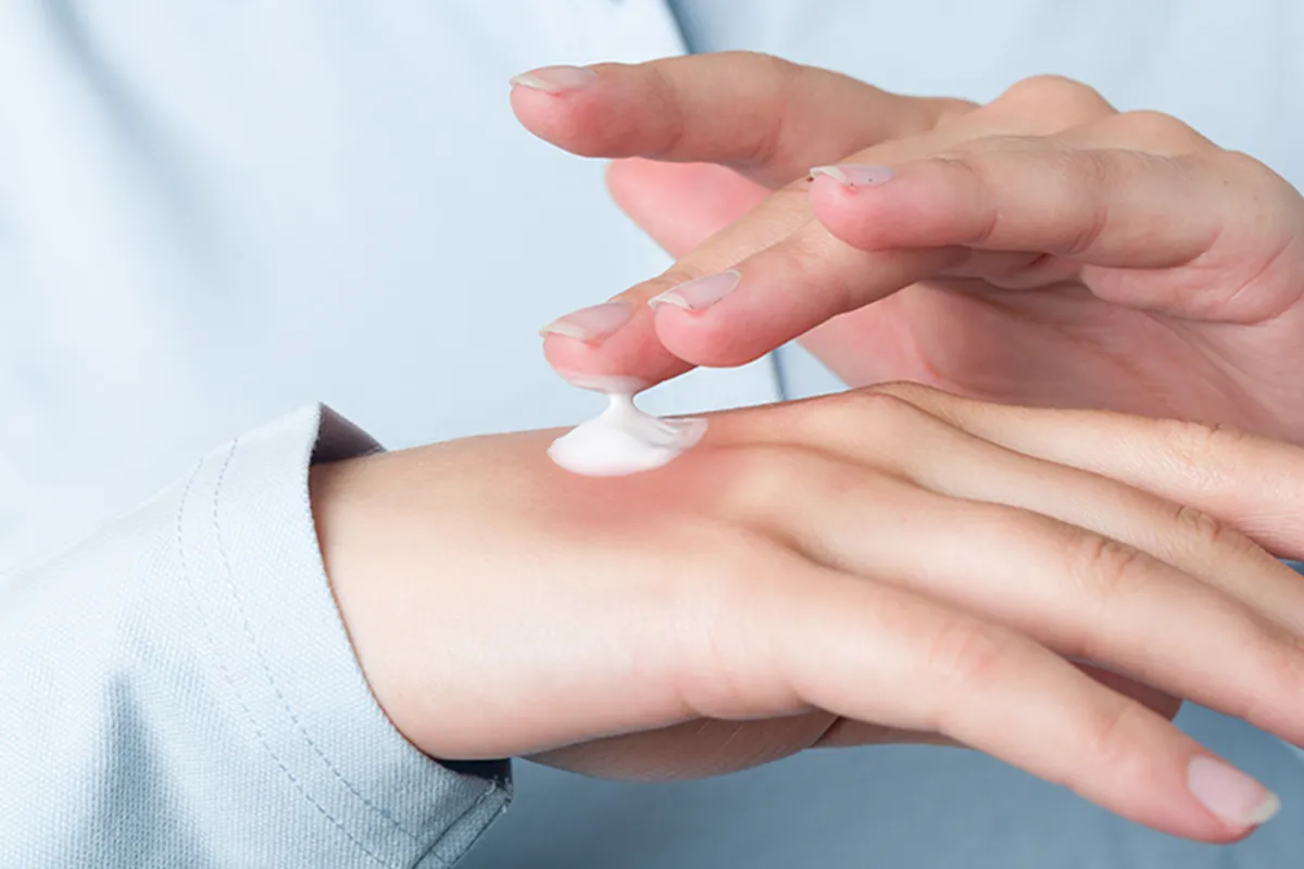 Ein dicker Tropfen Creme auf einem Handrücken mit einem Finger darüber