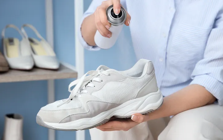 In einem Schuh wird ein Spray angewendet. Im Hintergrund ist ein Schuhregal zu sehen