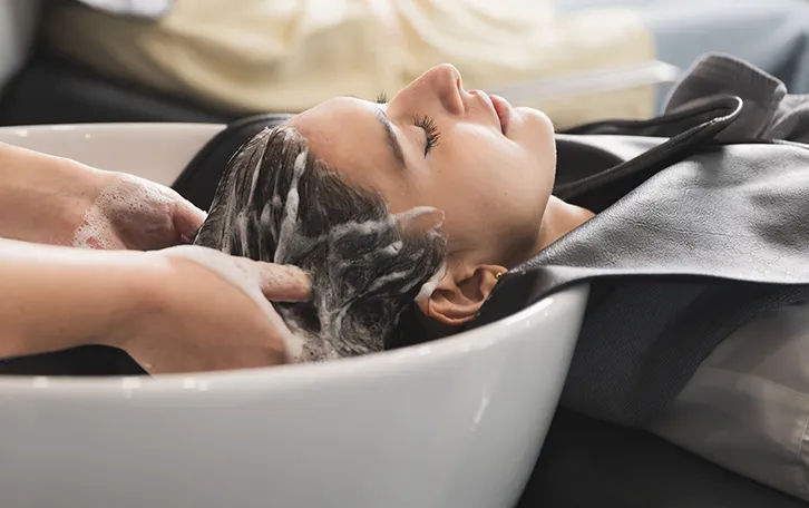 Einer weiblichen Person wird in einem Waschbecken die Haare gewaschen