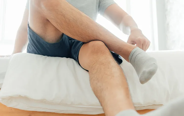 Eine sitzende männliche Person hat die eine Hand an ihrer Socke