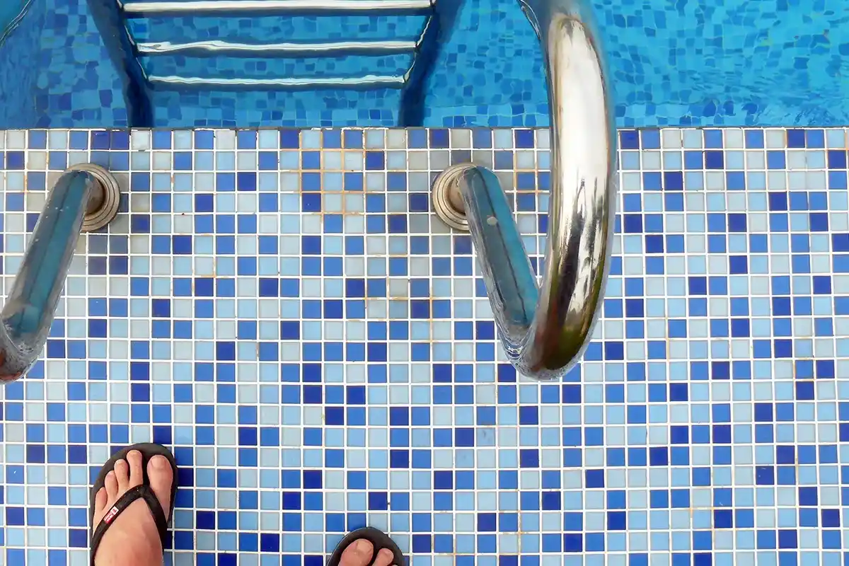 Pilzinfektion Nagelpilz Ansteckungsgefahr Der Einstiegsbereich eines in Blau gekachelten Schwimmbecken an einer Leiter mit Füssen in Flip Flops