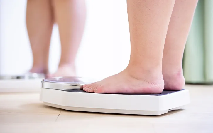 Jemand mit dickeren Beinen vor einem Spiegel auf einer Waage