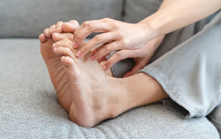Eine Person auf einer Couch liegend hat die Fingernägel auf den nackten Füssen angelegt
