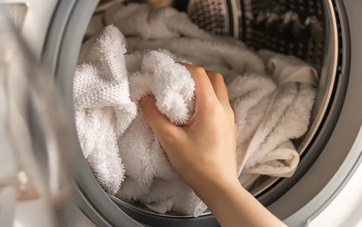 Eine Hand greift ein Handtuch welches in einer Waschtrollem zu sehen ist